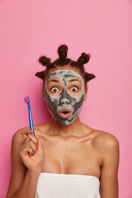 年轻化受惊的女人瞪着器的眼睛 拿着牙刷 摘下脸上的美容面膜后去刷牙 关心美容和卫生 赤裸的身体上戴着浴巾室内昏迷情绪