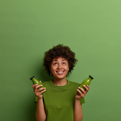 饮食快乐的非裔美国妇女持有冷健康混合饮料 浓缩以上 喝绿色素食蔬菜冰沙 在良好的状态 浓缩以上 微笑愉快超级食品的概念心情水果冰沙