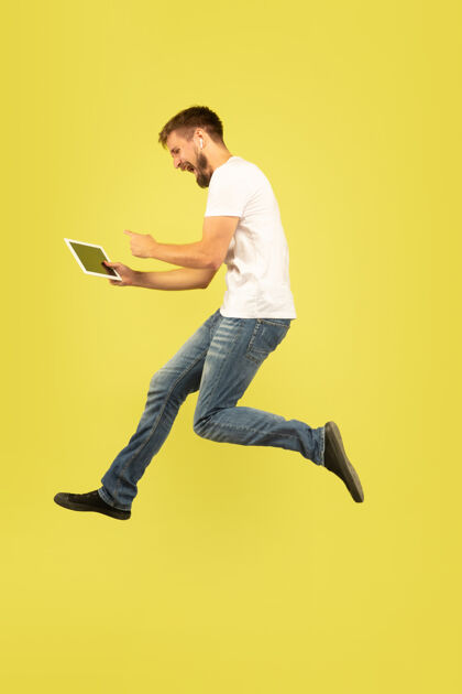 运动黄色背景上的快乐跳跃人的全长肖像手平板电脑男人