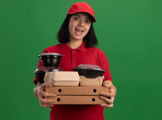 惊喜一个穿着红色制服 戴着帽子 拿着比萨饼盒和食品包的年轻送货女孩站在绿色的墙壁上 惊讶不已站着披萨年轻人