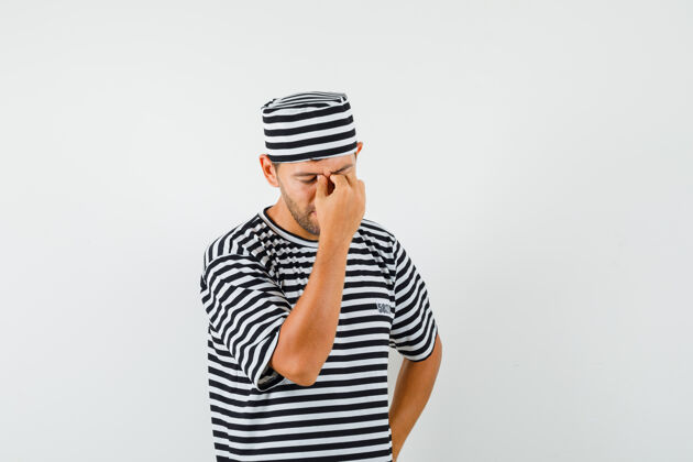 男性年轻男性戴着条纹t恤帽子揉眼睛和鼻子 看上去很疲惫科技网人类T恤
