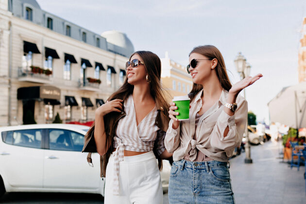 年轻两个白人女性朋友一边喝着咖啡一边聊天一边在城里散步成人朋友杯子