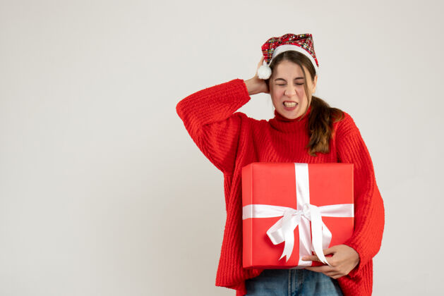 圣诞节前视图激动可爱的女孩戴着圣诞帽拿着礼物捂着耳朵站着礼物礼物圣诞老人