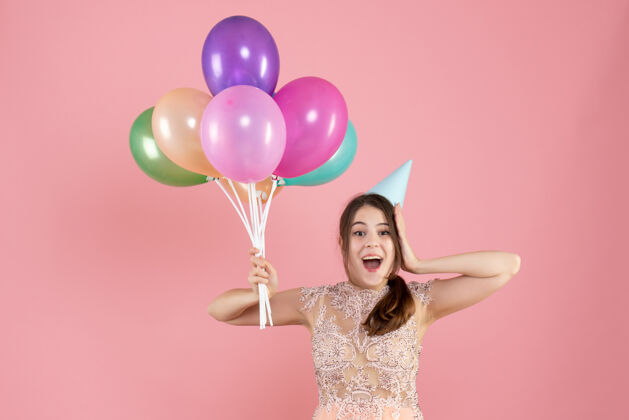 气球前视图兴高采烈的女孩与党帽举行彩色气球粉色丝带生日