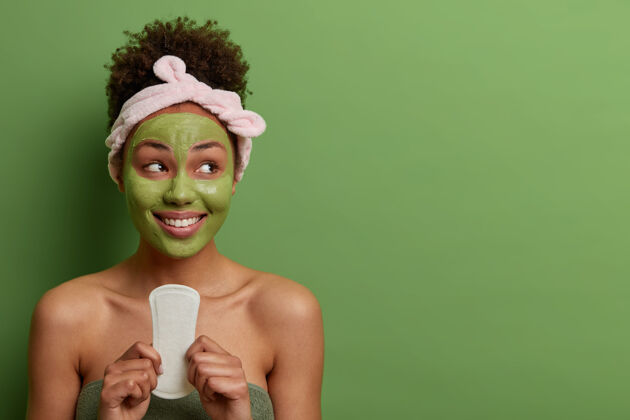 月经女人 卫生 美容 美容概念快乐快乐的女人拿着干净的卫生巾在月经期间使用 脸上带着牙齿般的微笑 隔离在绿色的墙上女人姿势干净
