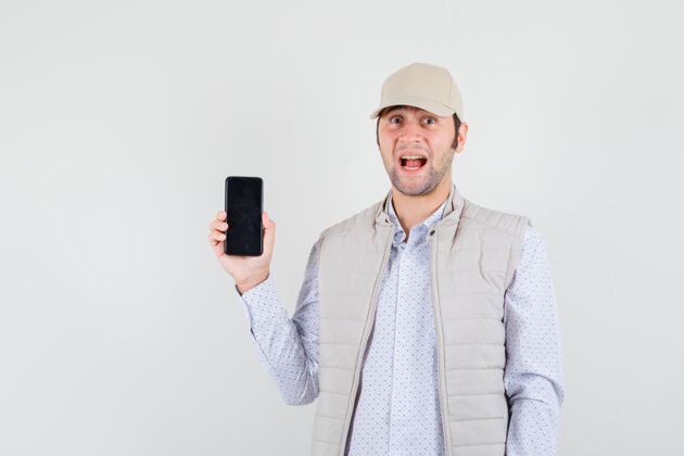 脸一个穿着米色夹克 戴着帽子的年轻人展示着手机 脸上露出惊讶的表情优雅人男人