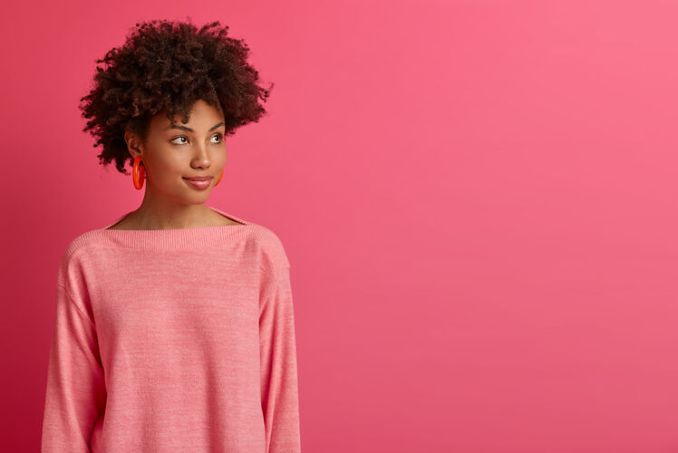 立场沉思的深色皮肤的非洲裔美国妇女的半身镜头转过去 集中在某个地方 考虑更好的方法 有一些想法 穿着长袖套头衫 孤立在粉红色的墙上女人正面沉思