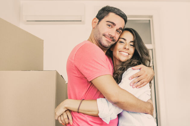 拉丁语快乐的夫妇搬进了新公寓 站在纸箱中间拥抱着房间变化成人
