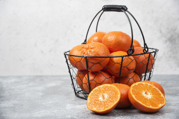 柑橘石桌上放着一个装满多汁橙子的金属黑色篮子成熟圆形多汁