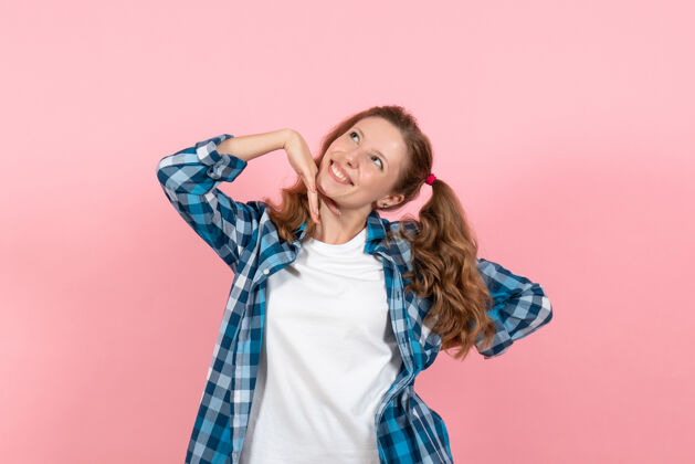 成人正面图身着蓝色格子衬衫的年轻女性在粉色背景上微笑摆姿势女性情感模特时尚女孩颜色情绪年轻女性格子