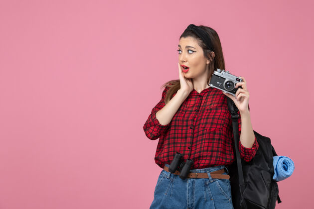 肖像前视图穿着红色衬衫的年轻女性 带相机 背景为粉色的照片 女模特人相机衣服