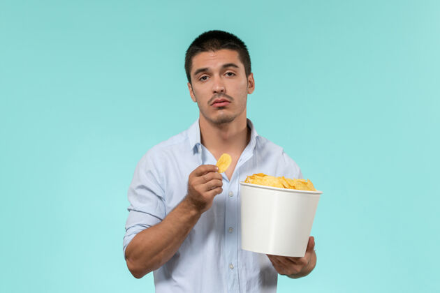 浅蓝色前视图年轻人拿着篮子和土豆cips在淡蓝色的墙上电影远程电影院电影肖像土豆