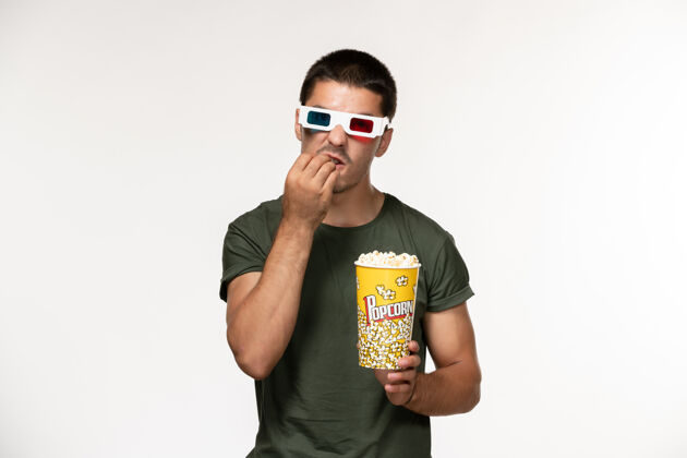 电影正面图身着绿色t恤 戴着d型太阳镜 手持爆米花的年轻男性在白墙上拍摄电影《孤独电影院》男性电影电影肖像年轻男性