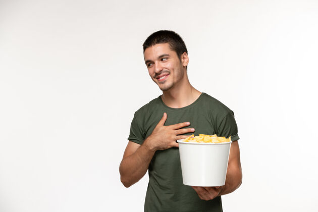 电影正面图：身穿绿色t恤的年轻男性 带着土豆cips 微笑着站在白墙上的电影人男性孤独电影电影院电影员工年轻男性
