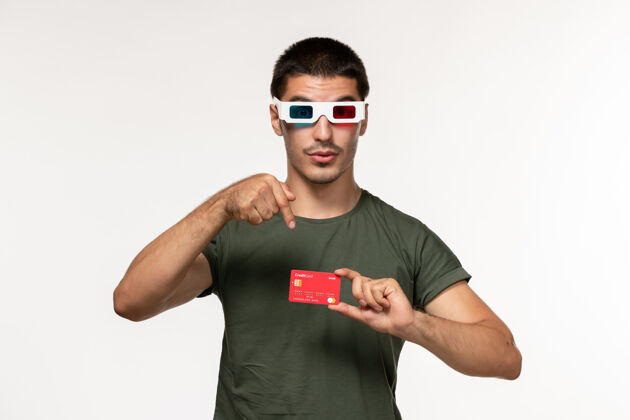 太阳镜正面图身着绿色t恤的年轻男子手持银行卡在白色墙上拍摄孤独电影院银行男人电影