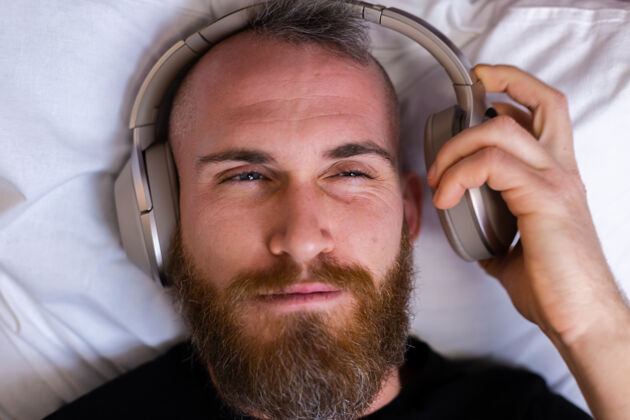 包装快乐的白人男子戴着耳机躺在床上听他最喜欢的音乐 独自休息 跳舞耳机移动科技