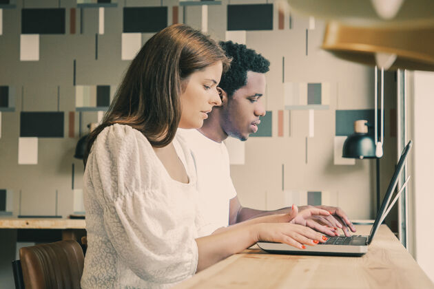 笔记本电脑多民族设计师坐在一起 在同一个工作空间工作的笔记本电脑女性开发沟通