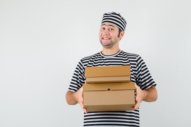 思想年轻男子穿着t恤 戴着帽子 手里拿着纸板箱 看上去很快乐 正前方的景色盒子脸休闲