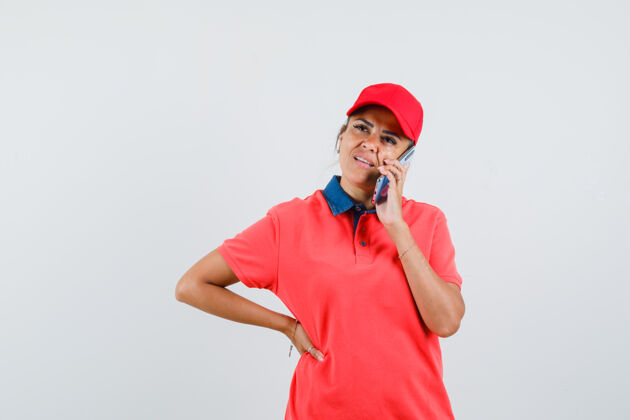 前面身穿红衬衫 戴着红帽子的年轻女子 手放在腰上 一边打电话 一边沉思着 前视图人女人沉思
