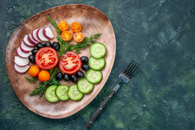 寿司上图：新鲜切碎的蔬菜橄榄放在一个棕色的盘子里 叉子放在绿黑色的混合色桌子上蔬菜午餐奇异果