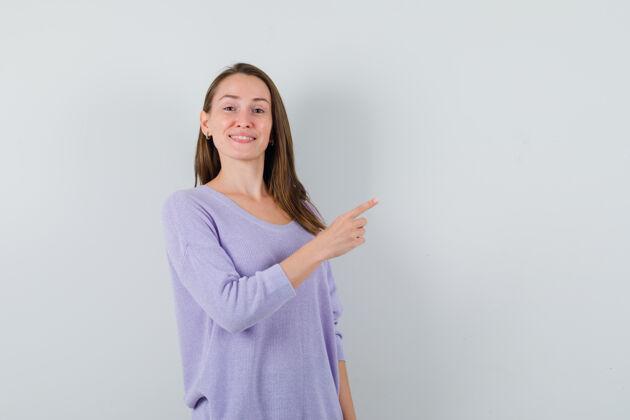 卷曲年轻的女性指着旁边的淡紫色衬衫 看起来很高兴漂亮女性指尖