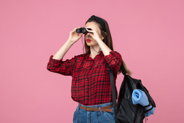 音乐家正面图穿红衬衫的年轻女性用望远镜在粉色背景上画学生色的女人望远镜麦克风年轻女性