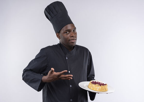 空间穿着厨师制服的年轻困惑的美国黑人厨师拿着并指着白色盘子上的蛋糕 上面留有复印空间复制混乱厨师