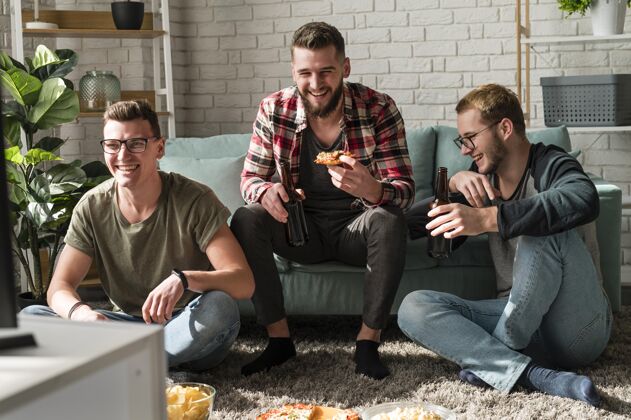 看电视笑脸男朋友吃比萨饼和看电视上的啤酒运动的正面图电视看电视最好的朋友