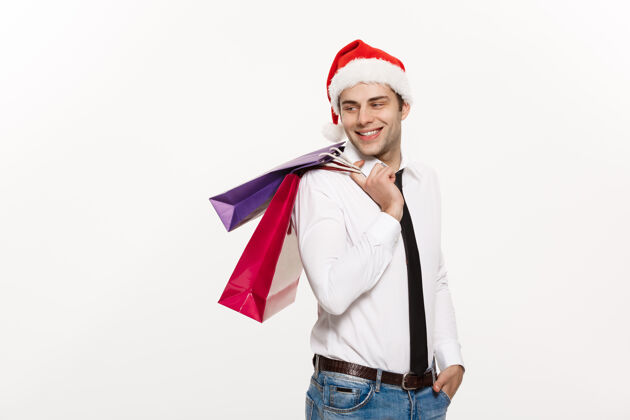 包英俊的商人戴着圣诞帽和购物袋庆祝圣诞快乐模型零售举行