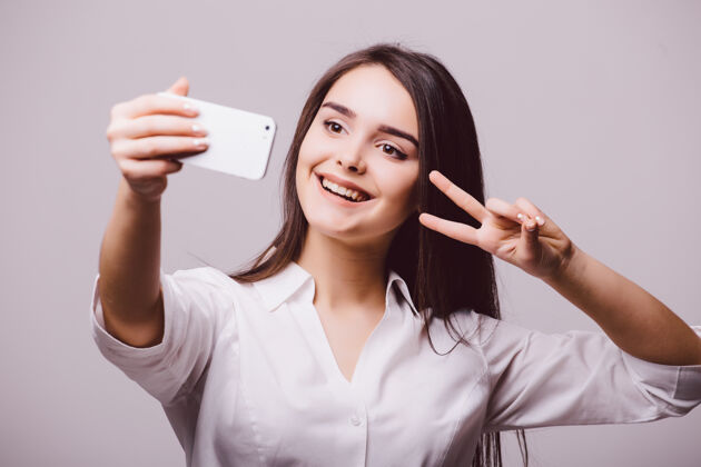 休闲一个微笑的可爱女人在智能手机上自拍的照片 白色背景上的隔离标志肖像手机