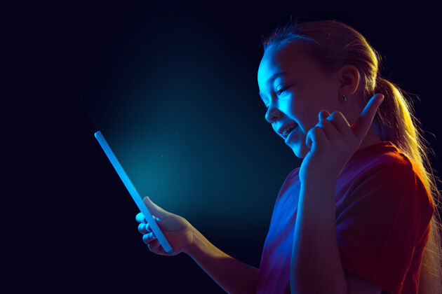 在线指着 大笑霓虹灯下黑墙上的白人女孩肖像使用平板电脑的漂亮女性模特人类情感的概念 面部表情 销售 广告 技术 小玩意梯度员工肖像