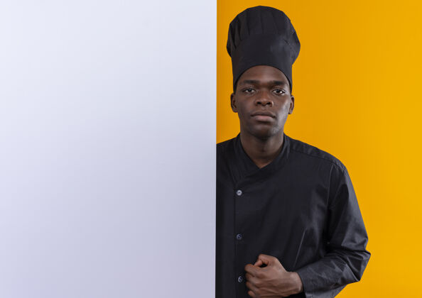 橙色年轻自信的美国黑人厨师身着厨师制服 站在橙色白色墙壁后 留有复印空间立场空间烹饪