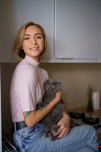 休闲微笑的女人在家里的厨房里和猫玩猫有乐趣感觉