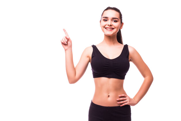 运动穿着运动服的快乐美丽的健身女士指着广告空间在白色背景上孤立微笑运动健身
