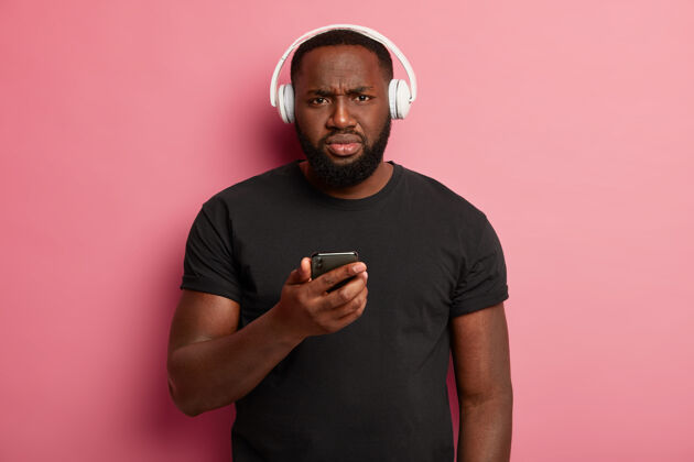 手机表情不悦的严肃黑人使用无线耳机丰满耳机音乐