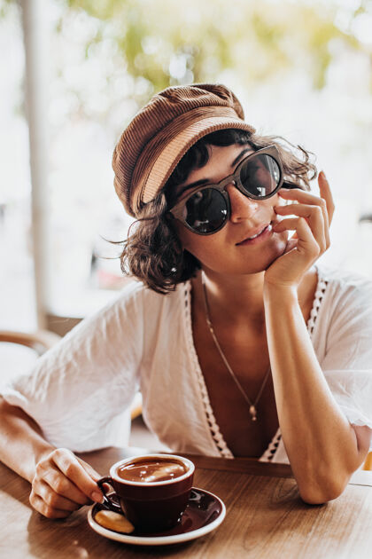 自然戴着棕色帽子和太阳镜的迷人女人在街边咖啡馆微笑咖啡馆餐馆漂亮