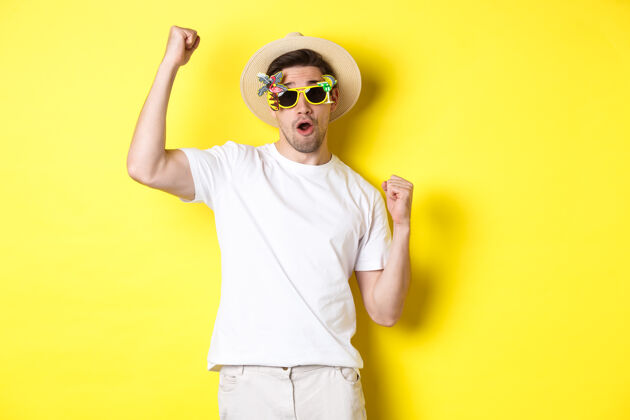 男人旅游和生活方式的概念快乐的家伙游客享受旅行 支持你 拳头泵和凯旋 在夏天的帽子和太阳镜 黄色背景的旅程时尚表情成年人