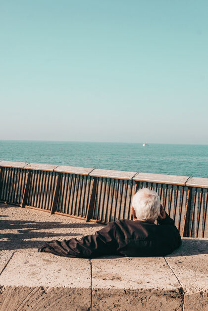 夹克白天 穿着黑色夹克的人坐在海边的棕色木凳上长凳放松大海