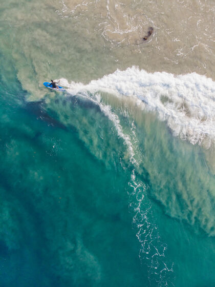 海岸线瓦卡拉海滩上一个人拿着冲浪板游泳的俯视图海洋度假村海滨