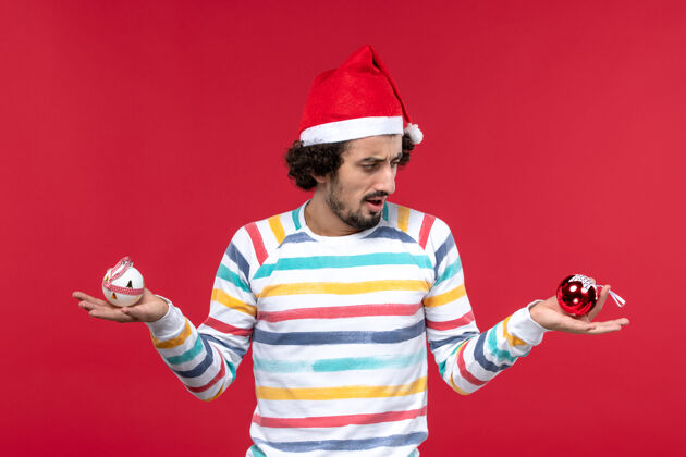 塑料正面图年轻人拿着塑料玩具站在红墙上红人过年前面圣诞节人