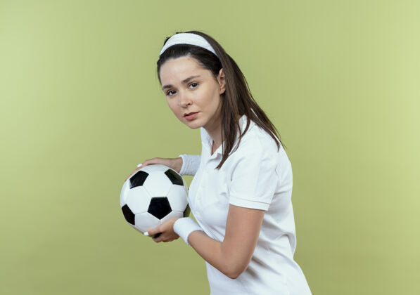 女子戴着头巾的年轻健身女 手拿足球 严肃的脸站在轻墙上立场健身球
