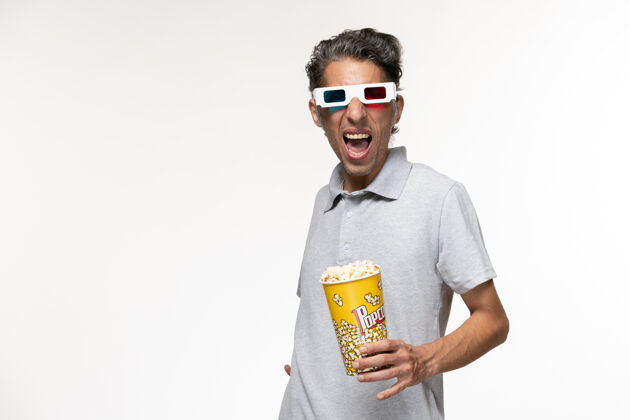 青少年正面图：戴着d型太阳镜在白色表面上吃爆米花的年轻男性太阳镜孤独电影
