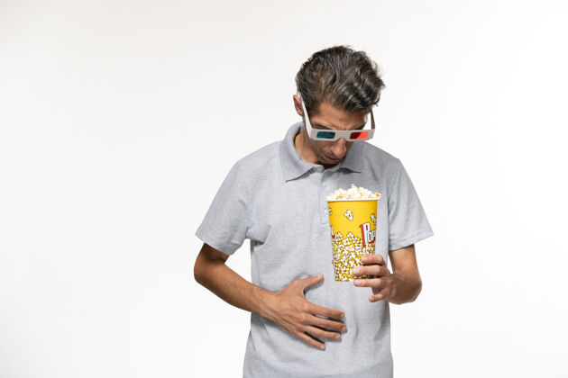 前面正面图白色表面上戴着d型太阳镜拿着爆米花的年轻男性孤独电影院抱着