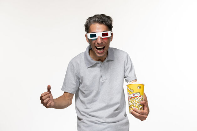 男性正面图：年轻男性戴着d型太阳镜在白色表面上吃爆米花看电影电影前面太阳镜