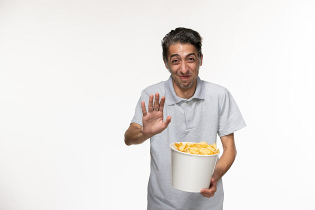 男正面图：年轻的男性在白色的表面上吃着薯片笑着孤独抱前面