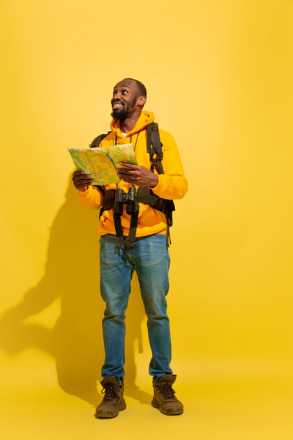 旅行一个快乐的年轻游客的肖像 带着包和望远镜 隔离在黄色的工作室墙上假期休闲度假村