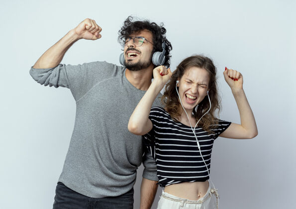 耳机年轻漂亮的夫妇戴着耳机站在白墙上欣赏音乐跳舞情侣年轻站立