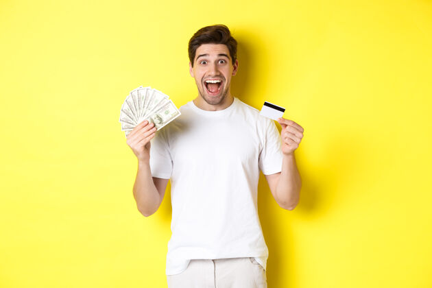 男人兴奋的男人准备好黑色星期五购物 拿着钱和信用卡 站在黄色的背景上有钱年轻金钱
