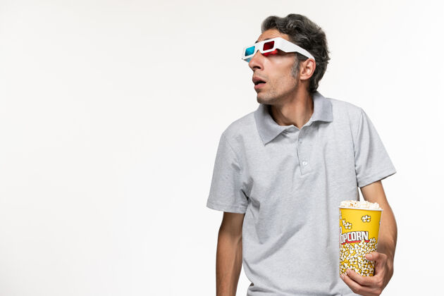 男正面图：年轻男性戴着d型太阳镜在白色表面上吃爆米花看电影孤独护目镜电影