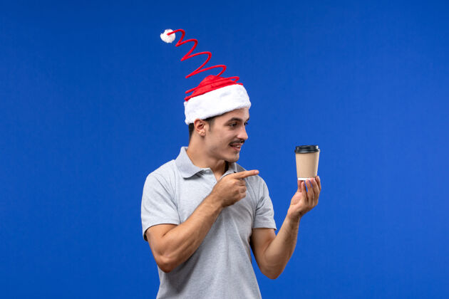 英俊正面图年轻男子拿着咖啡杯站在蓝色的墙上新年男子假期人咖啡人
